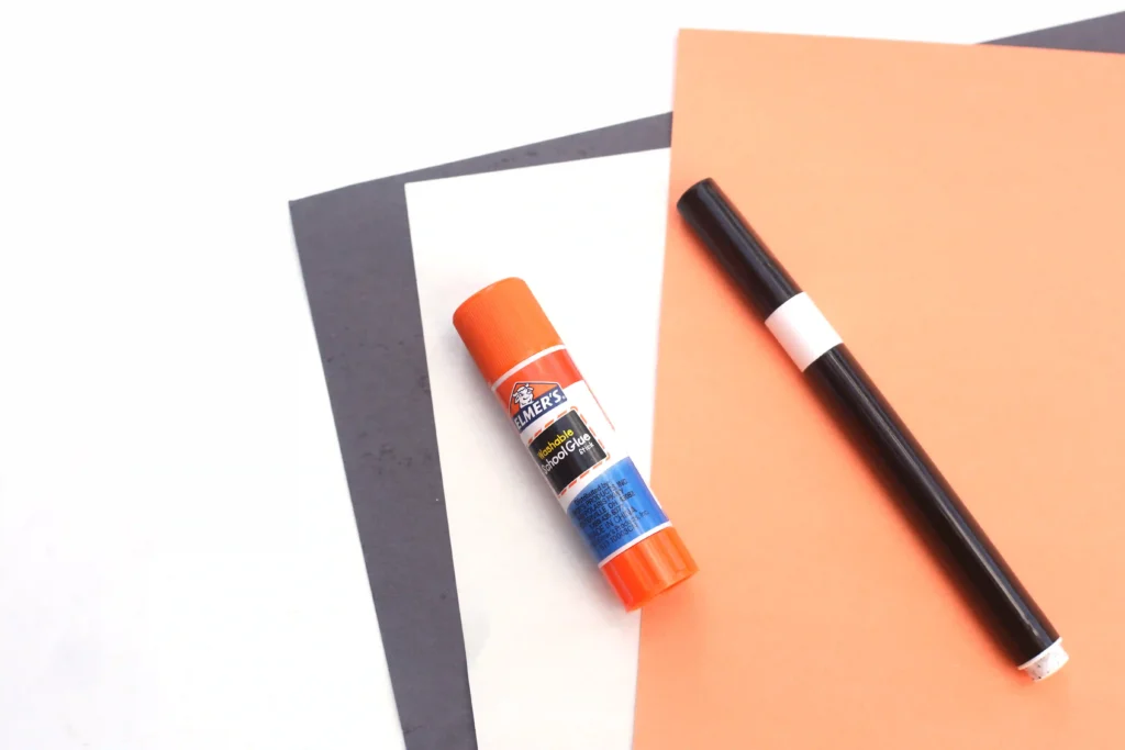 black, white, and orange construction paper, a glue stick, and a black marker