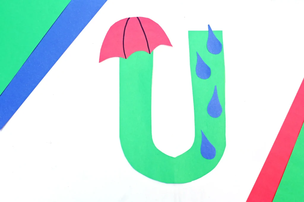 an uppercase U craft of the letter U cut out of green construction paper with an umbrella and rain drops glued on