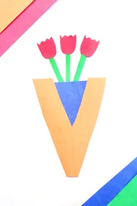 Three red paper tulips with green stems in a blue and orange letter V vase on a white background as an alphabet craft for kids