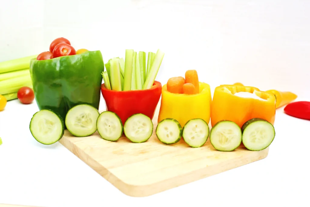 vegetables organized to look like a vegetable train that has various veggies inside bell peppers with cucumber slices for wheels