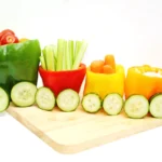 vegetables organized to look like a vegetable train that has various veggies inside bell peppers with cucumber slices for wheels