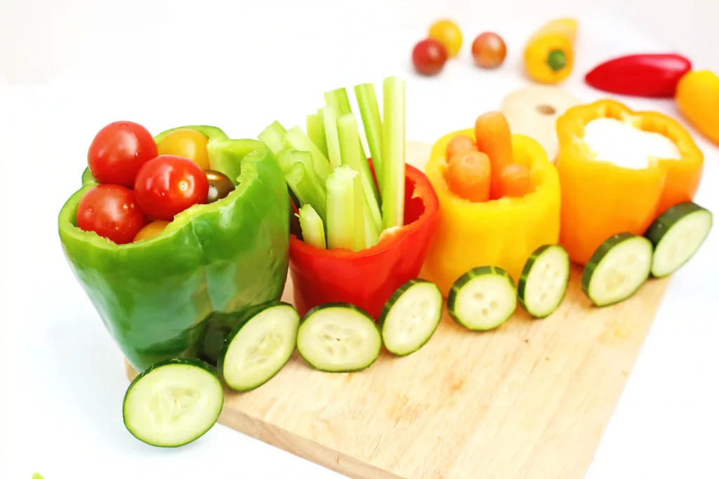 vegetables organized to look like a vegetable train that has various veggies inside bell peppers with cucumber slices for wheels
