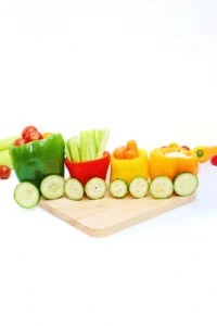 vegetables organized to look like a vegetable train that has various veggies inside bell peppers with cucumber slices for wheels