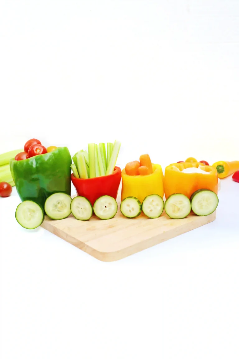 vegetables organized to look like a vegetable train that has various veggies inside bell peppers with cucumber slices for wheels