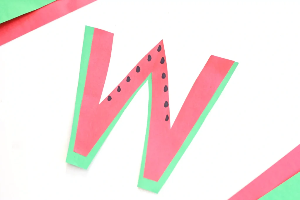 a watermelon craft for kids that has a letter w cut out of green and pink construction paper with black seeds drawn on