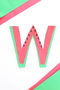 a letter w craft that has a letter w cut out of green and pink construction paper with black seeds drawn on