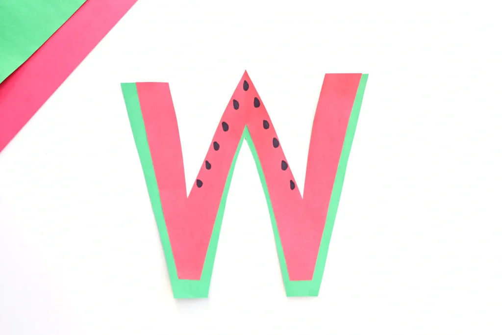 a preschool alphabet activity that has a letter w cut out of green and pink construction paper with black seeds drawn on
