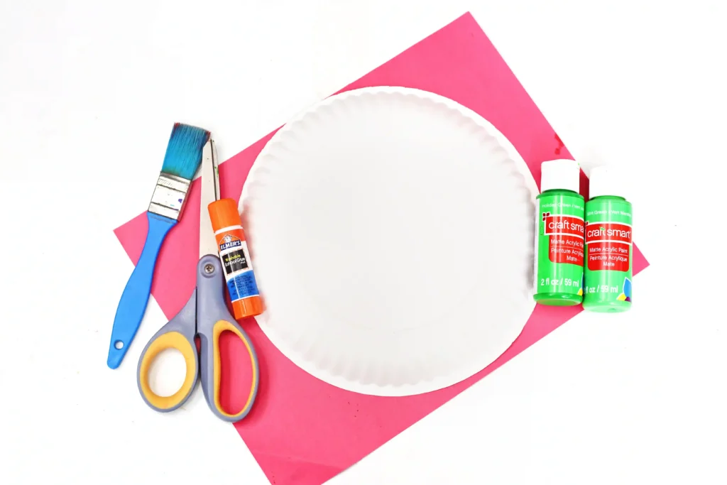 supplies for the Watermelon Jack-O-Lantern Paper Plate Craft - a paper plate, green paint, red construction paper, glue stick, scissors, and a paint brush