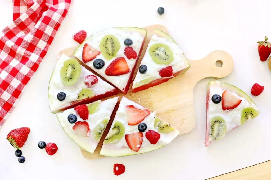 a watermelon pizza that is watermelon with whipped topping and fruits on top