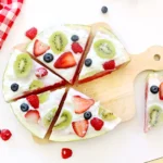 a watermelon pizza that is watermelon with whipped topping and fruits on top