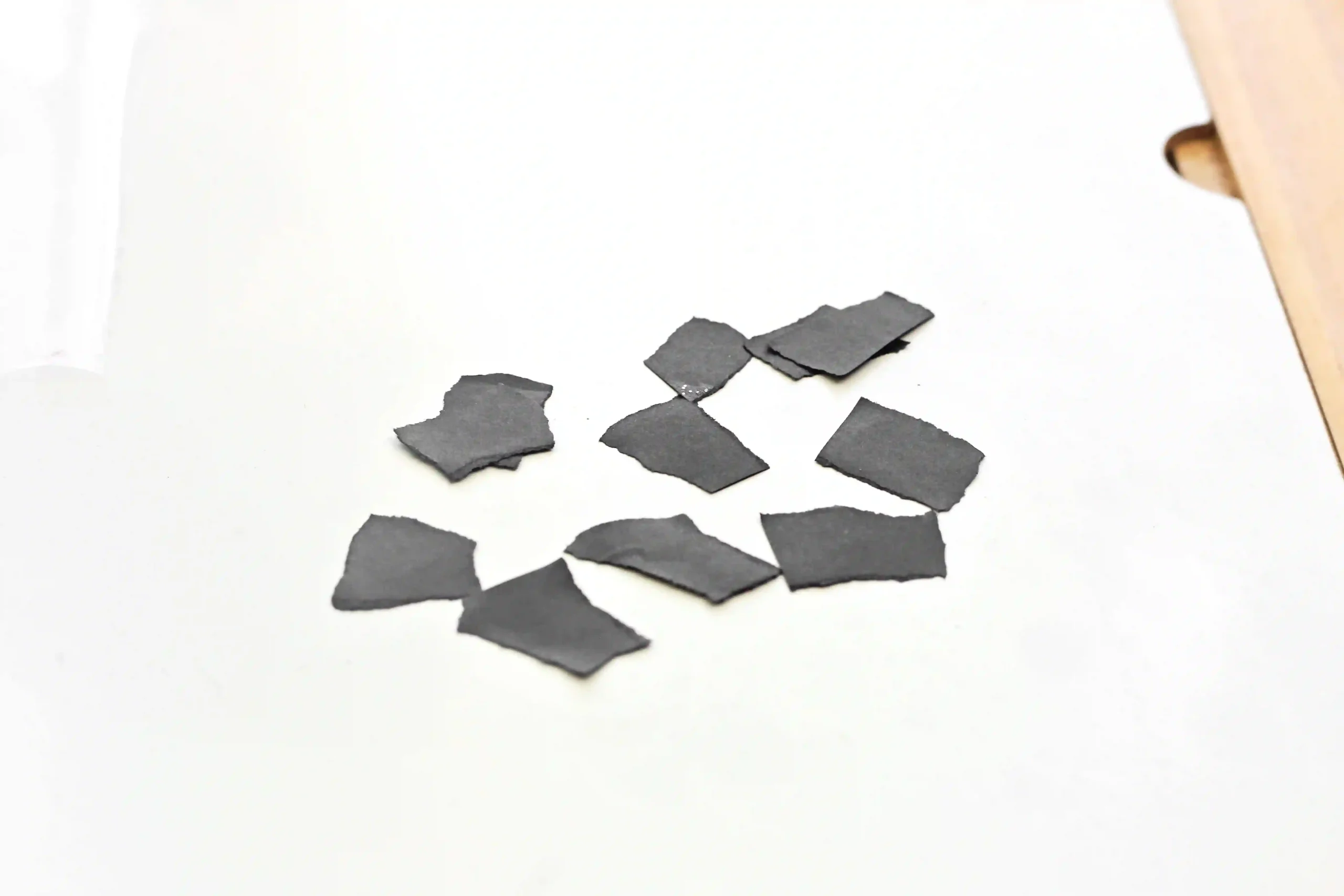 Several irregular black construction paper scraps scattered on a white surface.