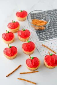 cupcakes that are decorated to look like apples with a pretzel stick for the stem and a green m&ms for the leaf to make these apple cupcakes