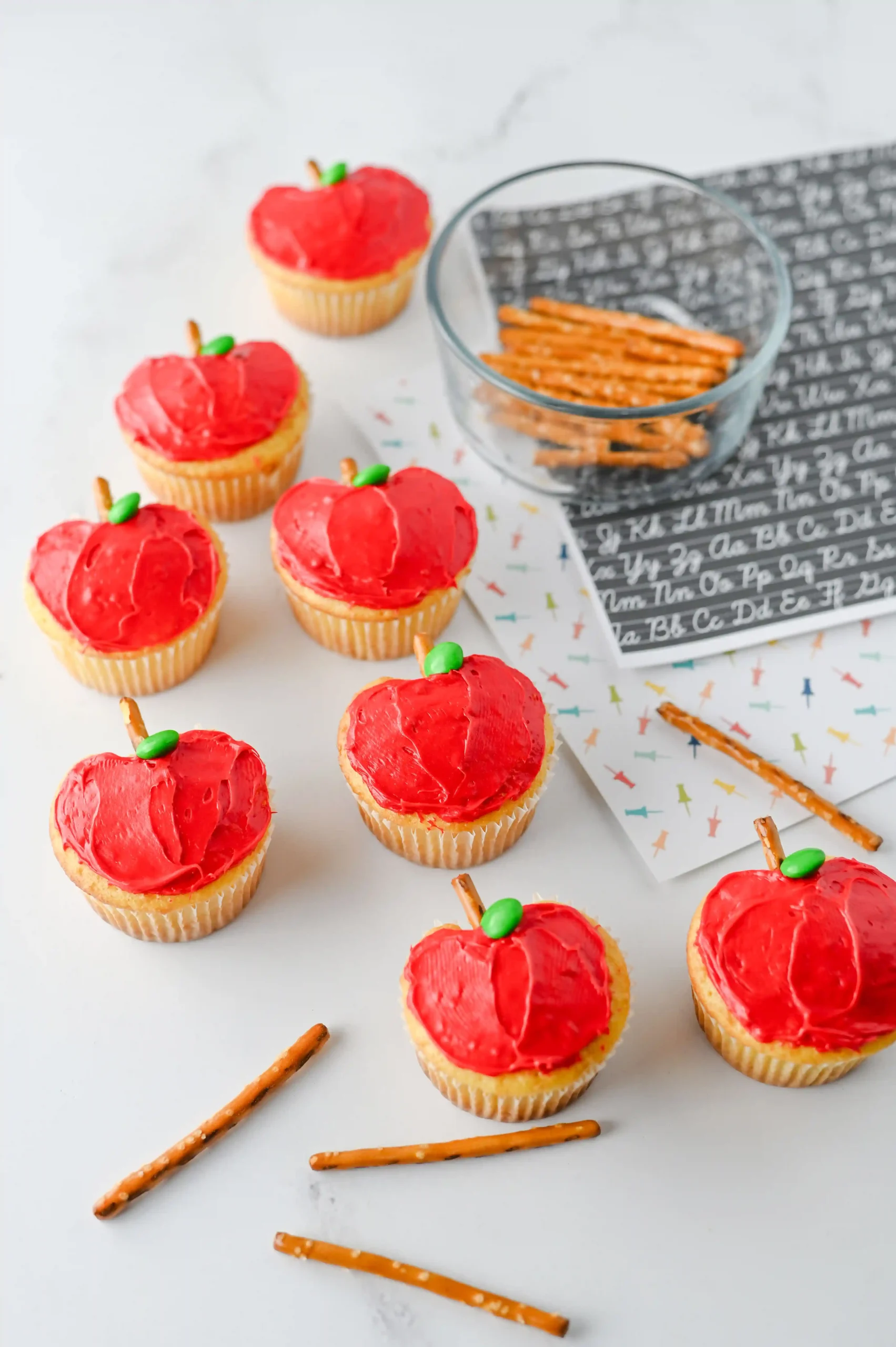 cupcakes that are decorated to look like apples with a pretzel stick for the stem and a green m&ms for the leaf to make these apple cupcakes
