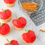 cupcakes that are decorated to look like apples with a pretzel stick for the stem and a green m&ms for the leaf to make these apple cupcakes
