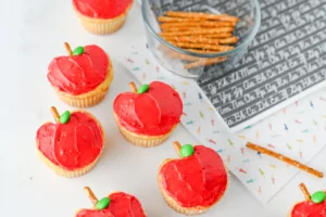 cupcakes that are decorated to look like apples with a pretzel stick for the stem and a green m&ms for the leaf to make these apple cupcakes
