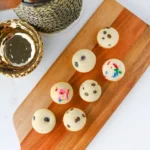 pancake bites with chocolate chips and colorful sprinkles arranged on a wooden serving board, with a metal basket in the background.