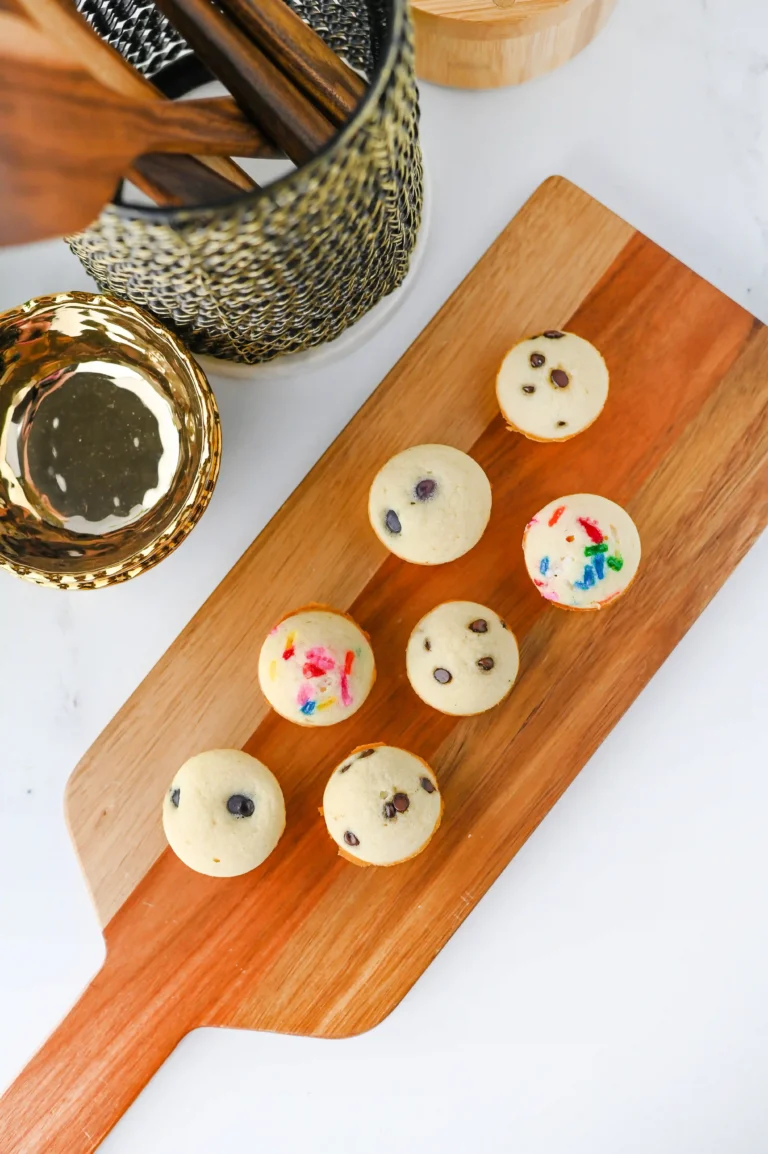 pancake bites with chocolate chips and colorful sprinkles arranged on a wooden serving board, with a metal basket in the background.