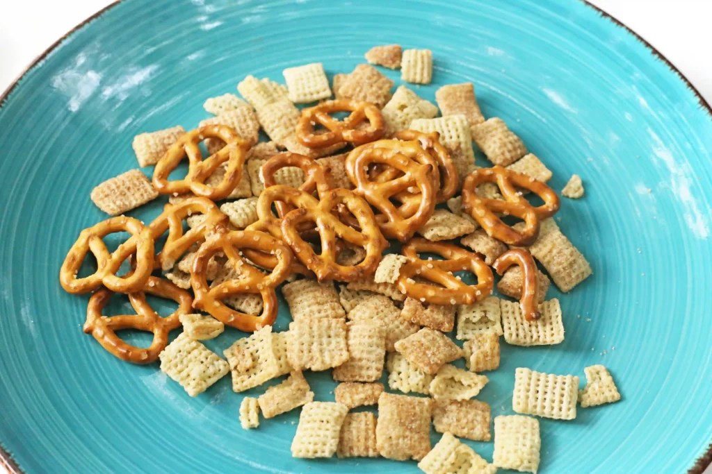 Turquoise plate scattered with chex mix and pretzel twists mixed together as a snack mix.