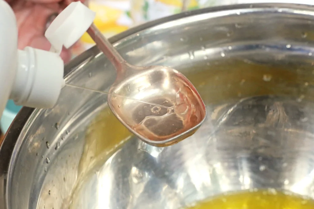 Lemon Slime - Cultivating Brilliant Minds Close-up of a metal ladle scooping saline solution into a large stainless pot in a kitchen setting.