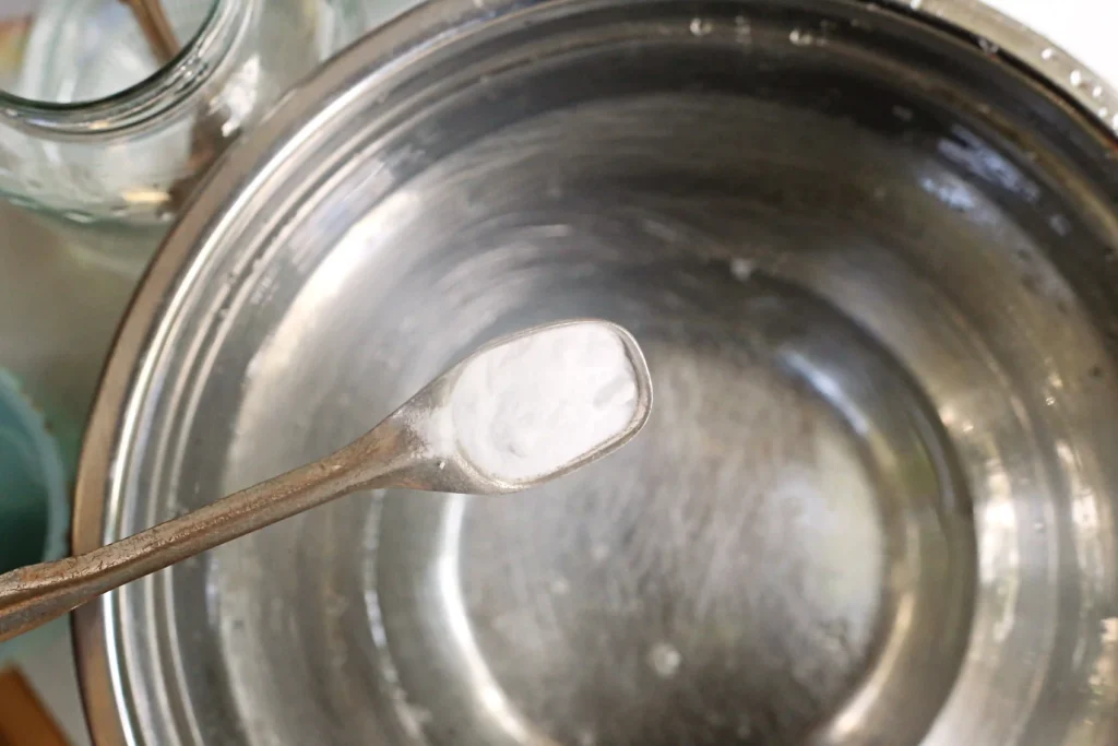 Lemon Slime - Cultivating Brilliant Minds a spoon with baking soda on it held over a mixing bowl with clear glue and water