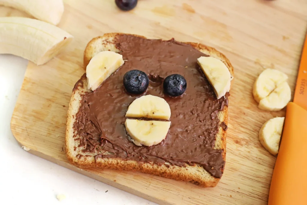 Toast with chocolate-spread, banana slices, and blueberries, made to look like a monkey face