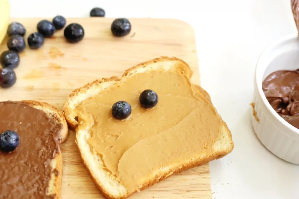 Toast slices with peanut butter and blueberries on a wooden cutting board for this toddler breakfast idea.