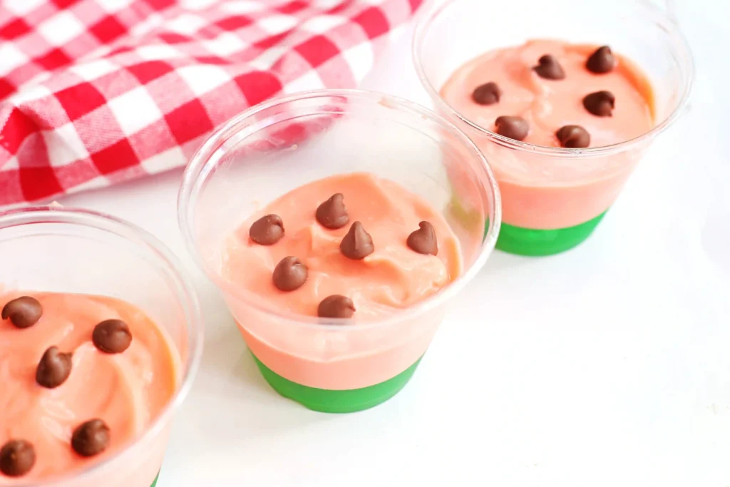 watermelon pudding cups with green jello and pink pudding with chocolate chips on top for an easy summer snack for kids