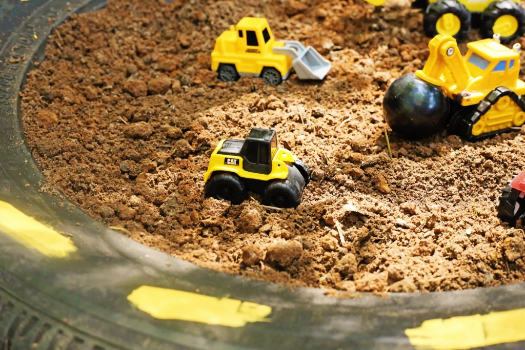 Yellow toy dump trucks and a loader in a dirt play area, tracing small construction scene in a sandbox-like surface