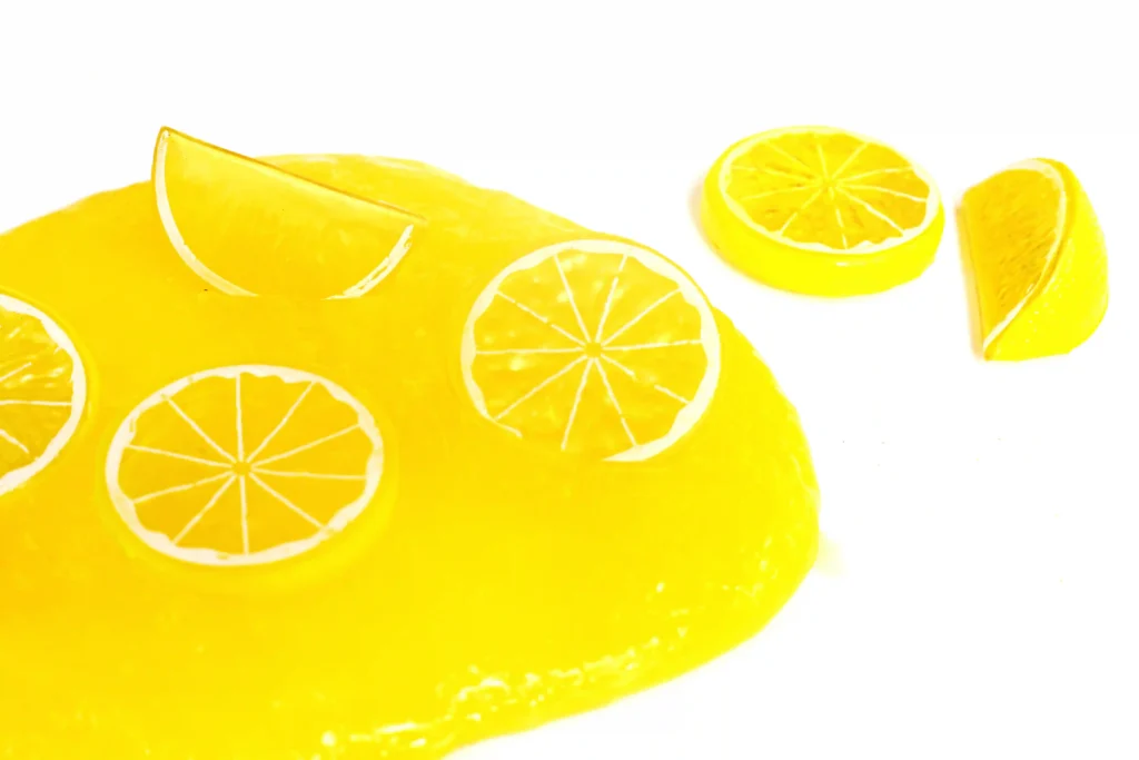 Lemon Slime - Cultivating Brilliant Minds Close-up of lemon slices arranged on a bright yellow slime with a white background behind them.