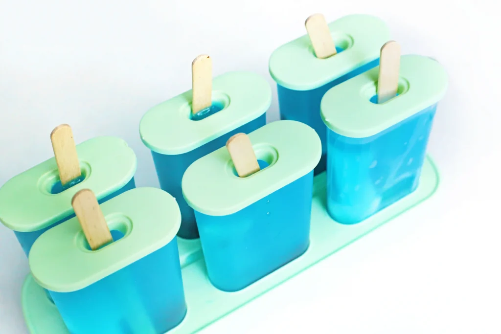 Row of blue and green summer popsicles in a popsicle mold with wooden sticks up front.