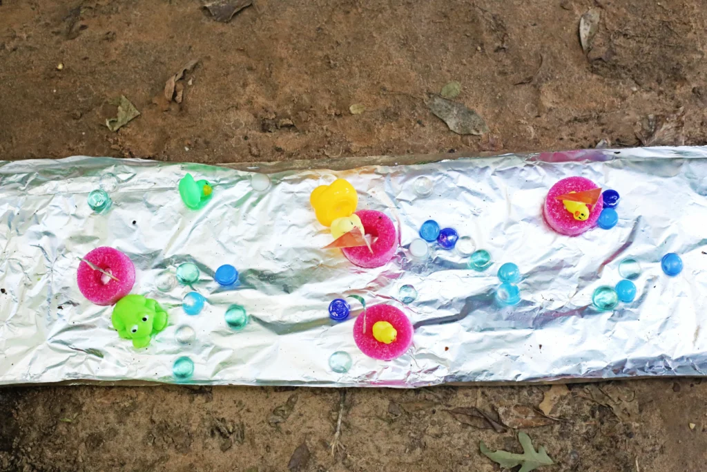 Aluminum Foil River - Cultivating Brilliant Minds an aluminum foil rive with pool noodle slices, rubber ducks, and clear flat rocks