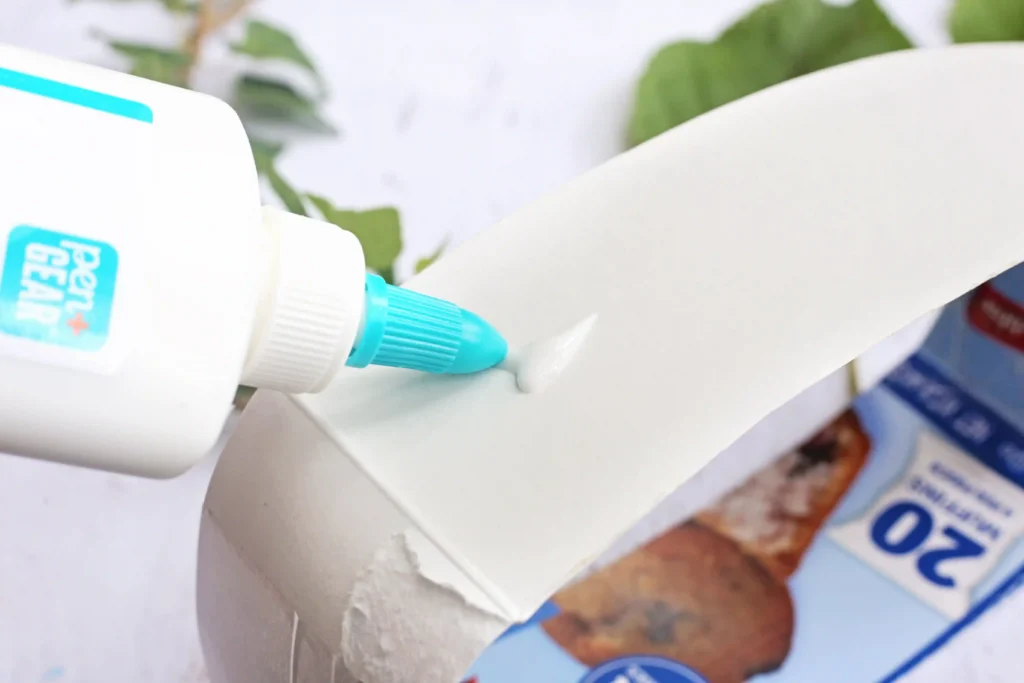 Leaf Crown - Cultivating Brilliant Minds Close-up of a white glue bottle squeezing glue onto a white surface, with a blue nozzle visible.