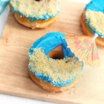 beach donuts that are glazed donuts with blue icing, crushed oreos for sand and a mini umbrella