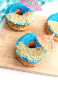 beach donuts that are glazed donuts with blue icing, crushed oreos for sand and a mini umbrella