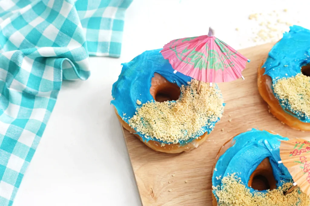beach donuts that are glazed donuts with blue icing, crushed oreos for sand and a mini umbrella