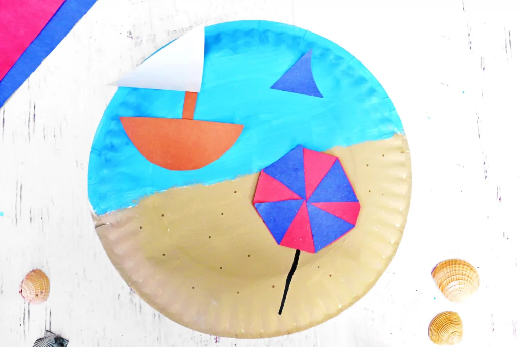 a Beach Paper Plate Craft that is a paper plate painted half blue half tan with construction paper umbrella and sail boat