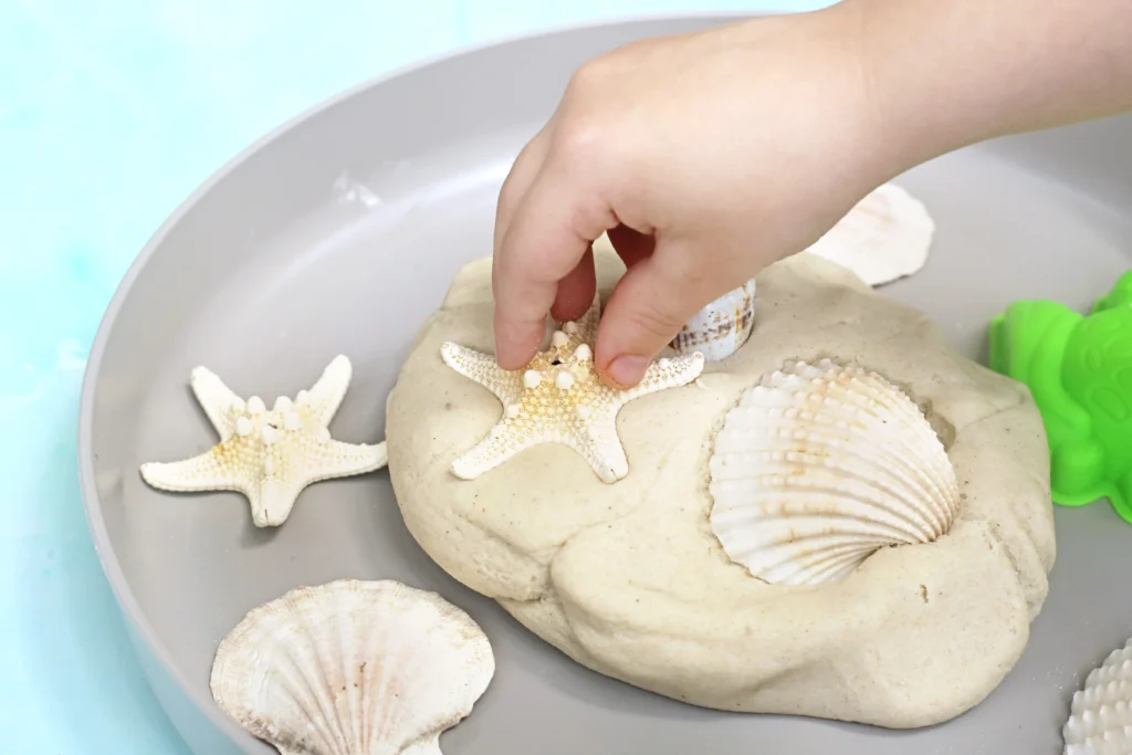 a kid pressing seashells into sand paydough