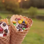 S'mores recipe that have marshmallows, chocolate chips, and m&ms in a waffle cone