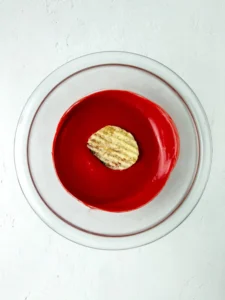 Top-down view of a round glass bowl with bright red melted chocolate and a single chip on top for this back to school snack