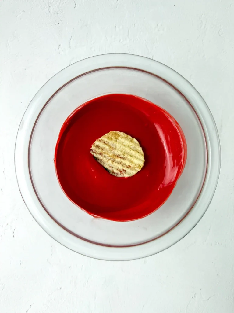 Chocolate Covered Apple Chips - Cultivating Brilliant Minds Top-down view of a round glass bowl with bright red melted chocolate and a single chip on top for this back to school snack