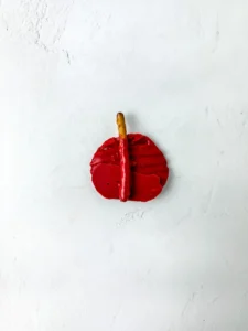 A single red chocolate covered chip with a short brown pretzel stem on a pale, textured white surface for this back to school dessert