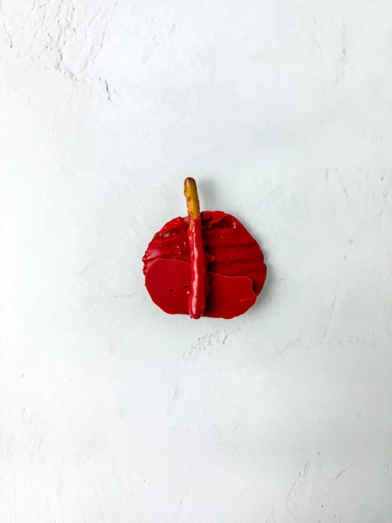 Chocolate Covered Apple Chips - Cultivating Brilliant Minds A single red chocolate covered chip with a short brown pretzel stem on a pale, textured white surface for this back to school dessert