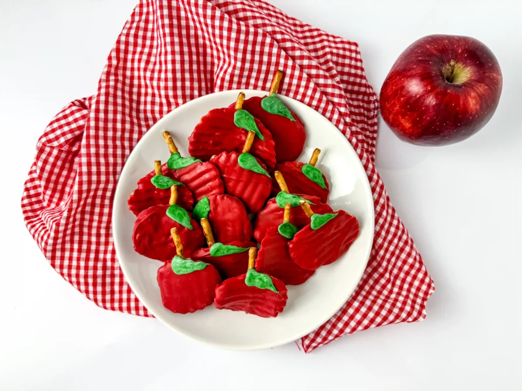 Chocolate Covered Apple Chips - Cultivating Brilliant Minds Chocolate Covered Apple Chips that are chips covered with red melting chocolate with a pretzel rod for a stem and a green melting chocolate leaf