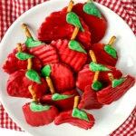Chocolate Covered Apple Chips that are chips covered with red melting chocolate with a pretzel rod for a stem and a green melting chocolate leaf on a white plate for a back to school dessert board