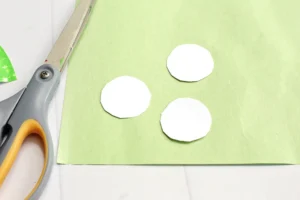 Scissors on a green workspace with several white circular paper cutouts for a craft project.