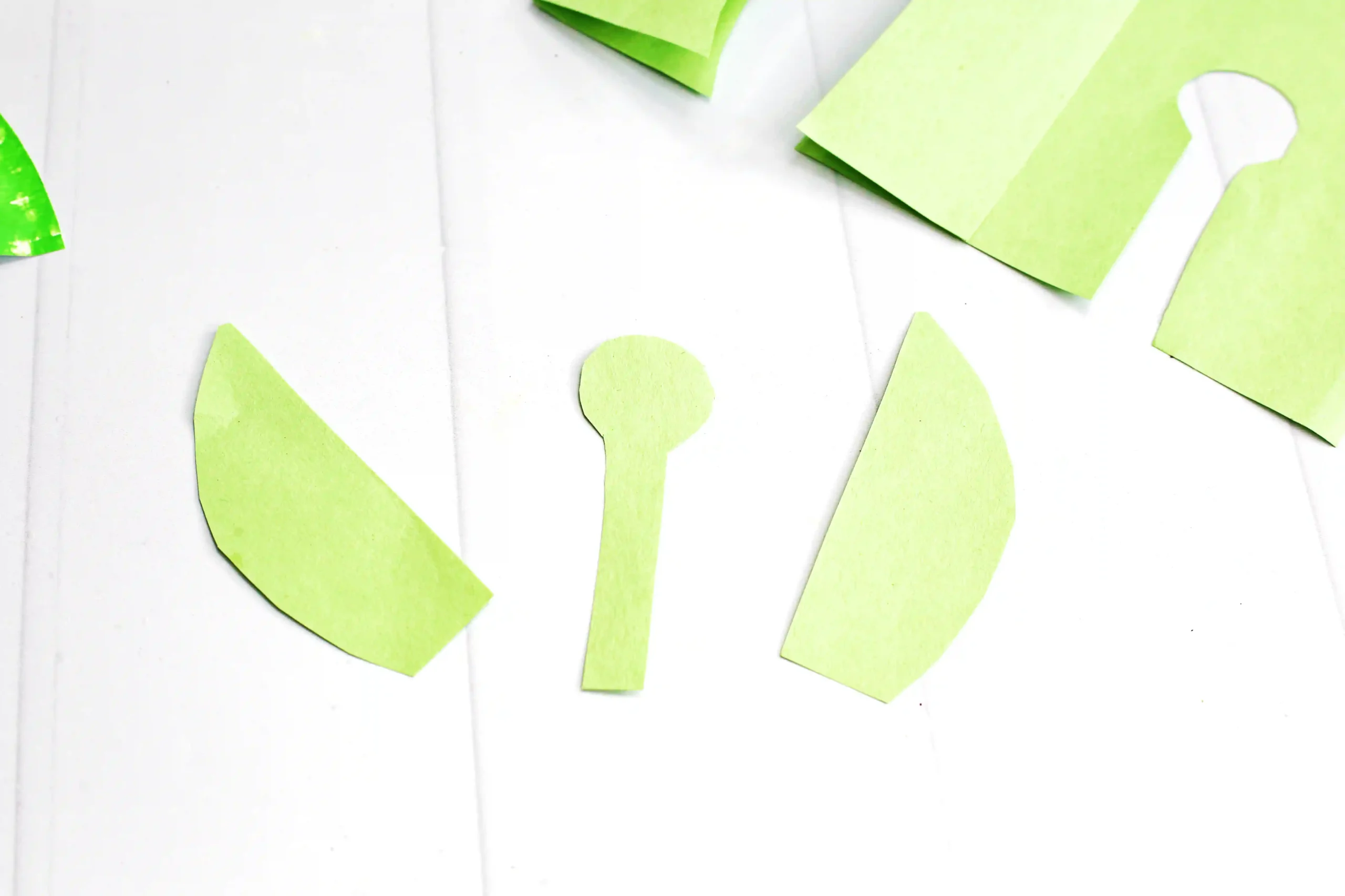 Lime-green paper scraps scattered on a white wooden surface in an abstract craft layout