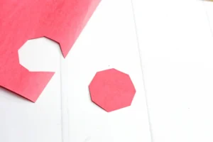 Close-up of pink hexagonal paper cutouts on a white surface, some edges showing folds.