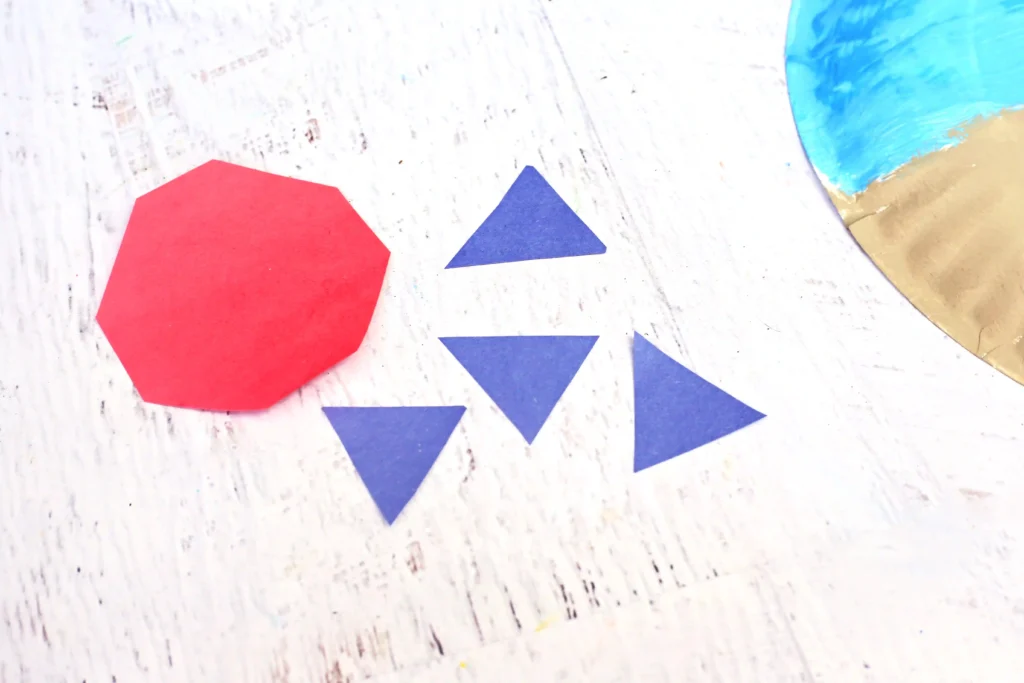 Red octagon and blue triangles cut from paper laid on a white, wood-textured surface.