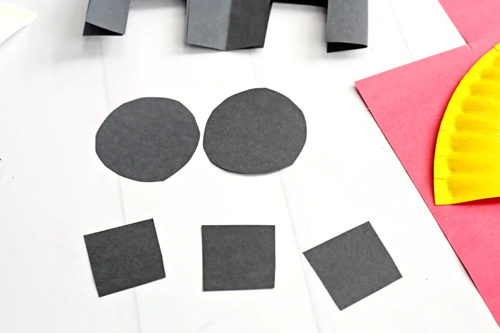 Abstract paper collage: two dark gray circles and several dark gray squares on a white background with pink and yellow accents.