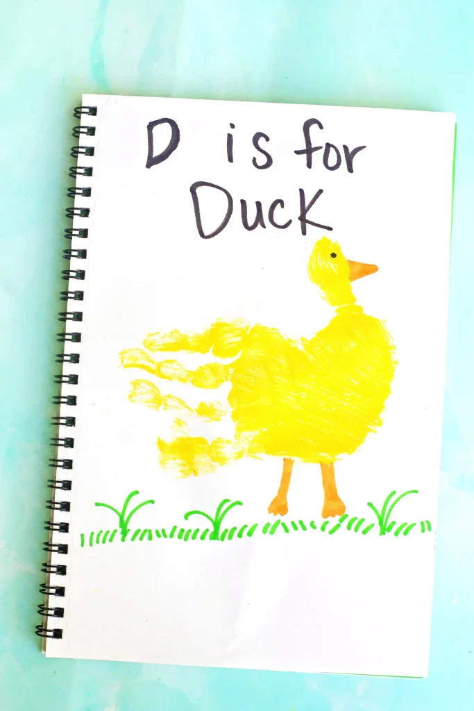 Letter D Duck Handprint Craft - Cultivating Brilliant Minds Notebook page with handwriting'D is for Duck' beside a yellow duck illustration on green grass and a turquoise background.